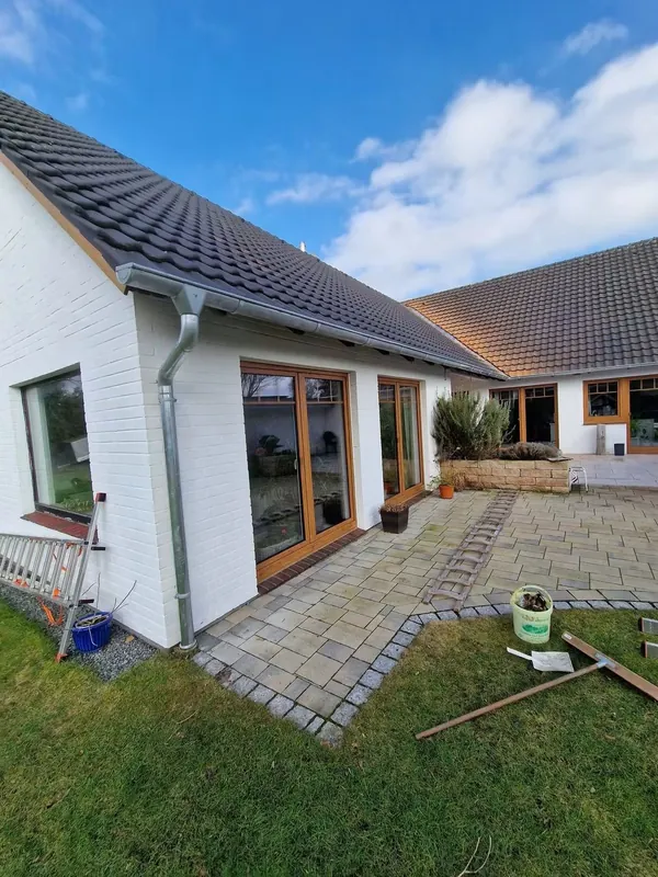 Bungalow mit neuer Rinne und Fallrohr, davor eine gepflasterte Terrasse