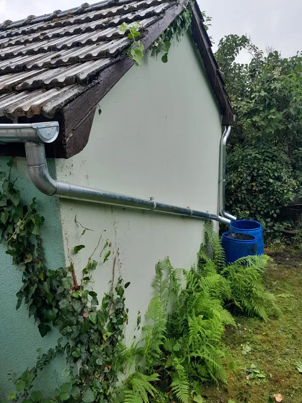 Neues Fallrohr am Giebel eines Gartenhauses, unten eine Regentonne