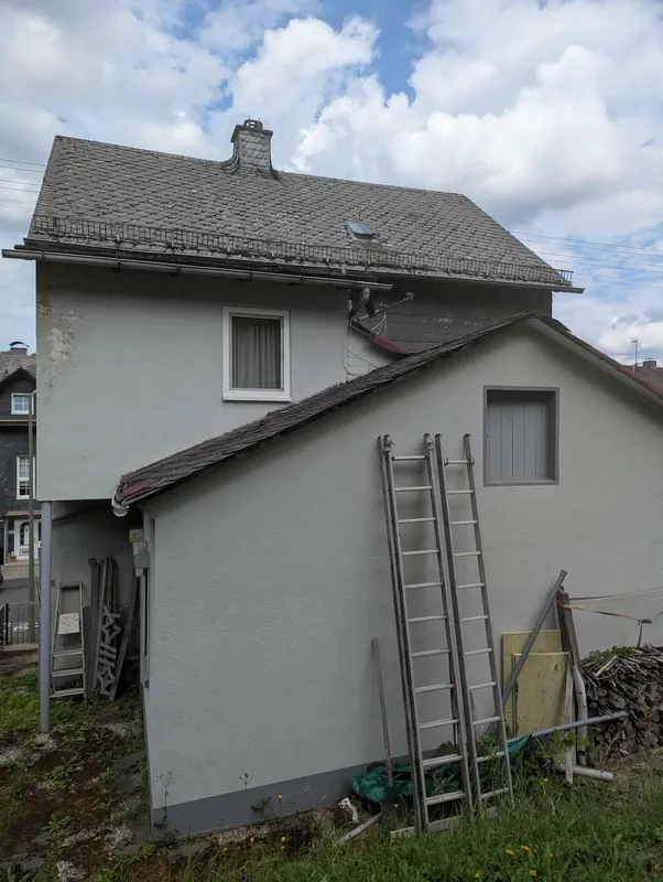 Giebel eines Wohnhauses mit neuem Fallrohr, daneben eine angelehnte Leiter
