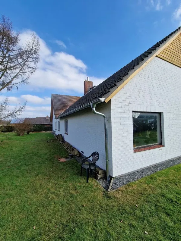 Weißes Wohnhaus mit neuer Dachrinne, davor eine Rasenfläche