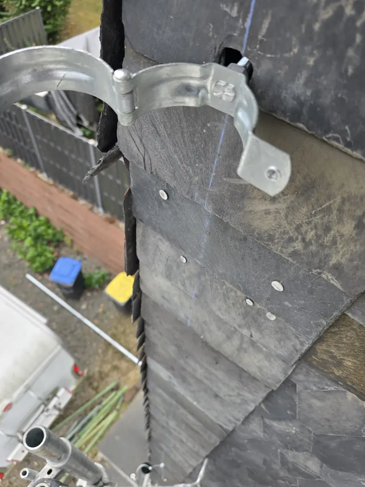 Neuer Rinnenhalter aus Metall, auf einem Schieferdach verschraubt