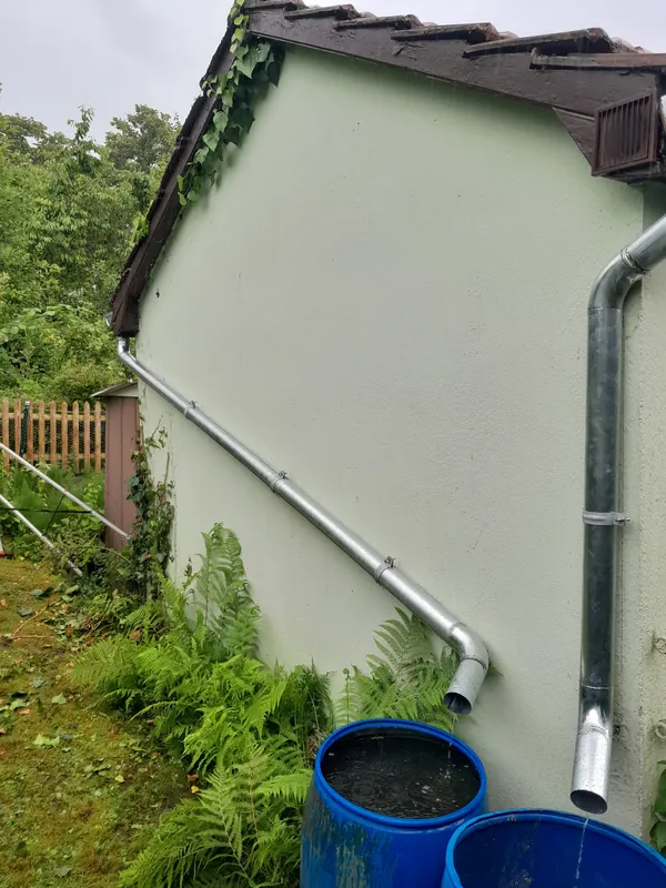 Giebel eines Gartenhauses mit neuer Rinne und Fallrohr, das in Regentonnen läuft